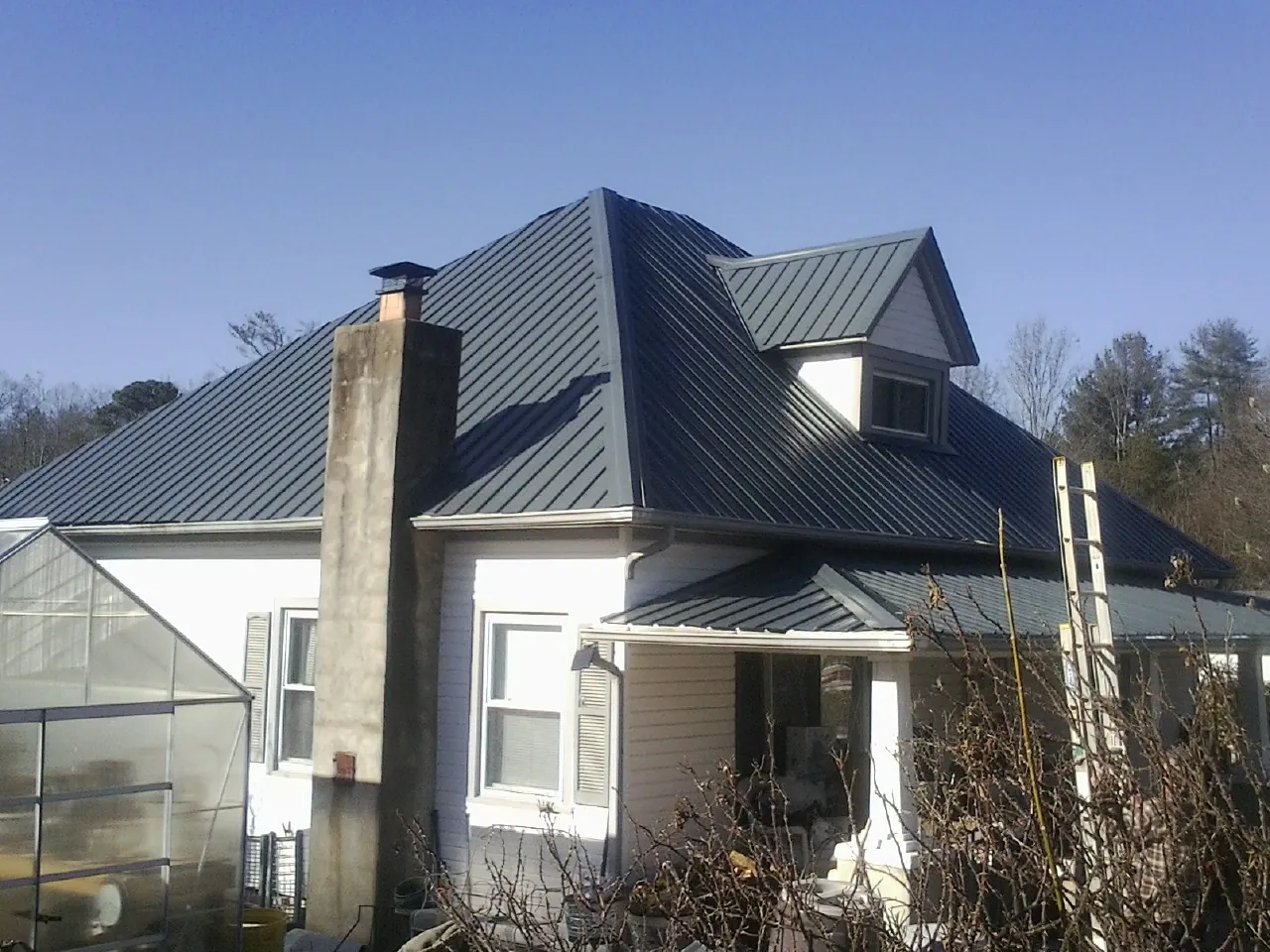 Dark blue standing seam metal roof on a white farmhouse with dormer — Slate & Tile Roof Repair by Roofing Brothers in Gallatin