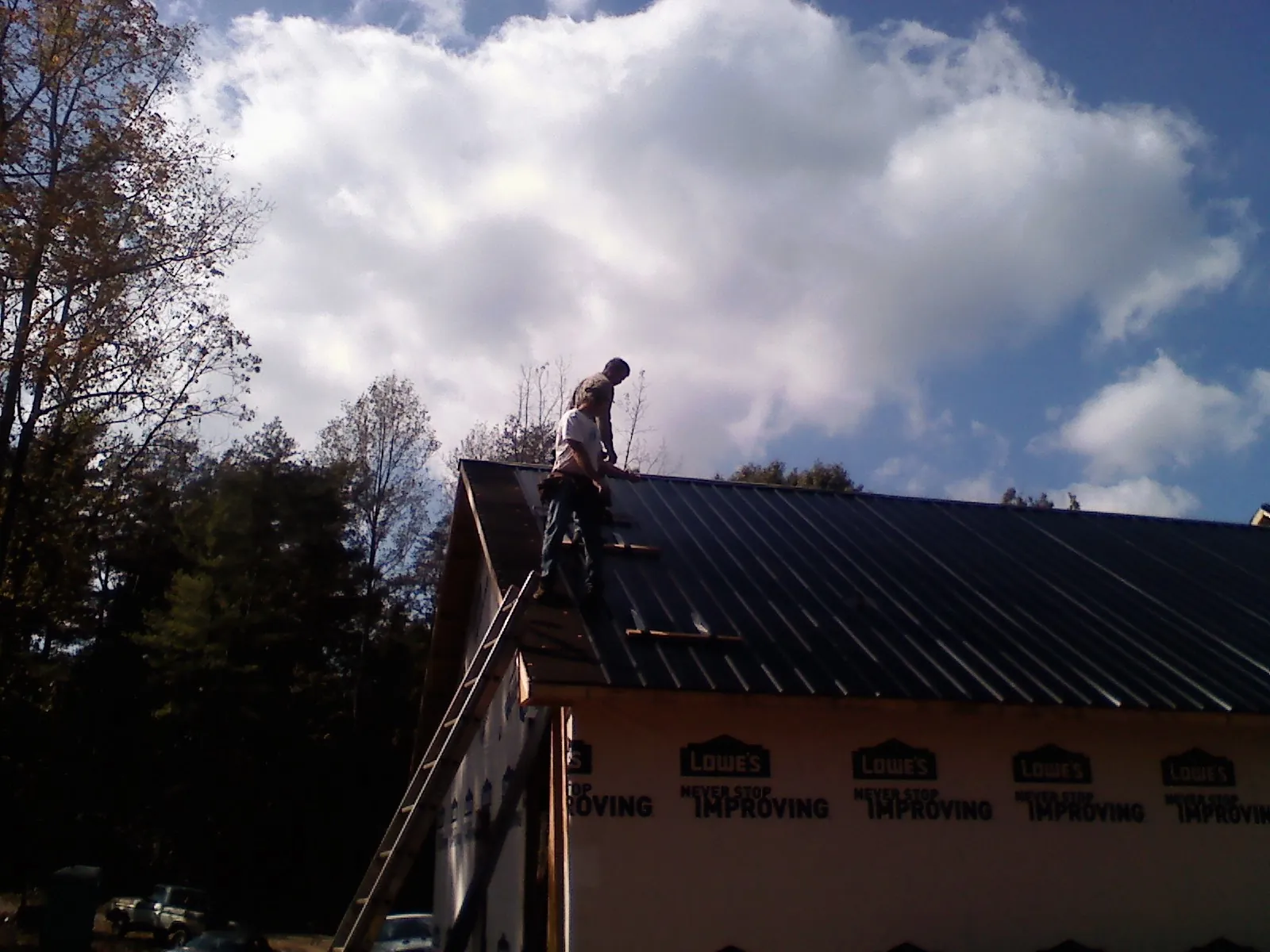 Roofer fastening dark metal panels high against a cloudy sky, from a Roof Inspection job in Gallatin